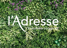 l'Adresse Immobilier Coopératif sur Mur Végétal Vert Logo l'Adresse l'immobilier coopératif blanc sur un fond de plantes vertes et fleurs mauves.
