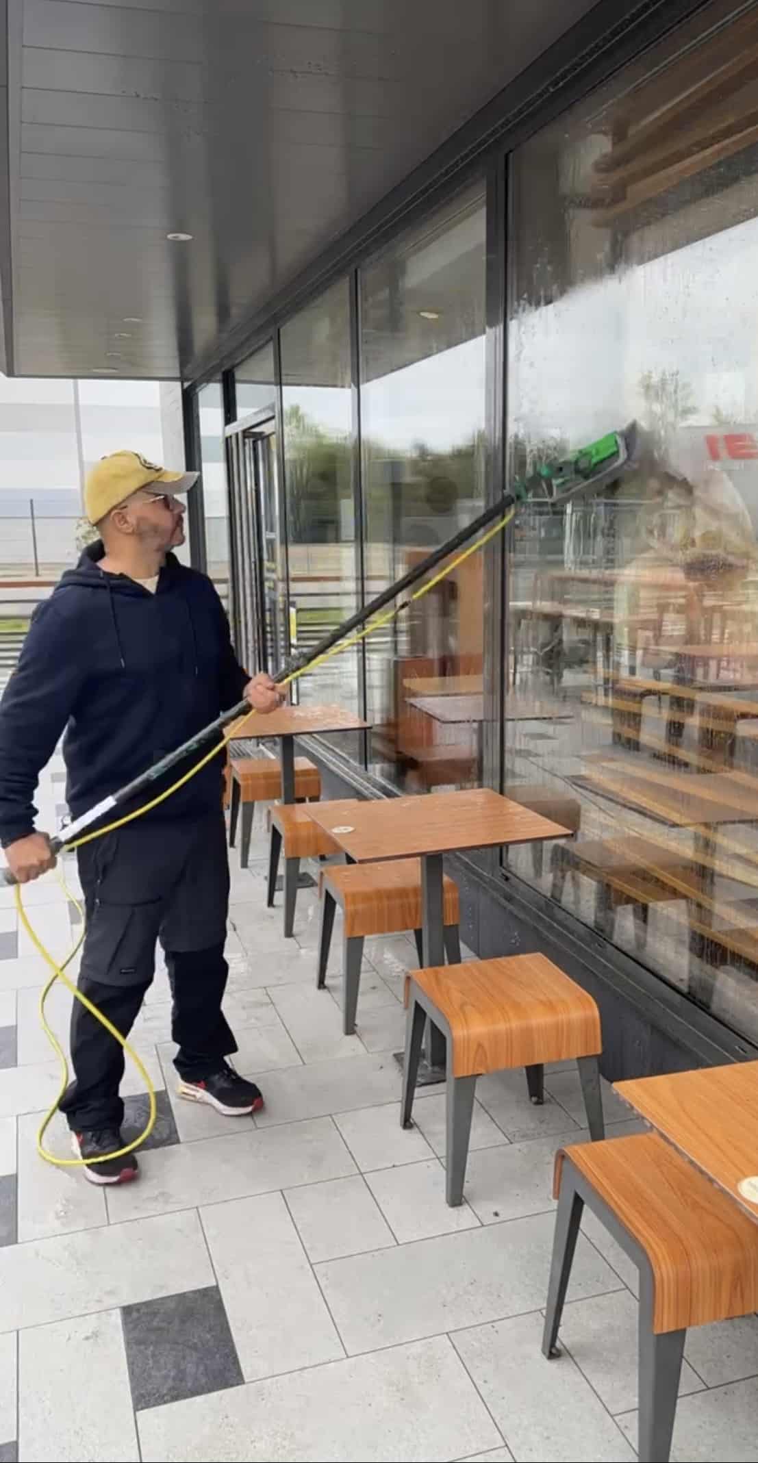 Nettoyage de Vitres Professionnel avec Perche Télescopique Laveur de vitres professionnel utilisant une perche télescopique pour nettoyer la devanture d'un restaurant.